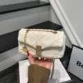Bolso acolchado crema en primer plano, sostenido a mano, con cadena dorada, cierre y colgante redondo - Blanco
