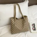 Vista oblicua de un bolso beige con lunares blancos y dos asas, sobre ropa de cama blanca - Caqui