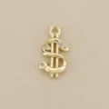 Close-up of a gold dollar-sign pendant with clear stones and a loop, laid on beige fabric - Gold
