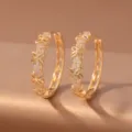 Close-up of gold-tone hoop earrings with openwork four-petal flowers and sparkling clear stones - White Flower (E1921) / Gold and White