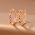 Close-up of paired gold-tone hoop earrings with openwork flowers and red accents on fabric - Rose Red Flower (E1920) / Gold & Rose Red