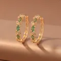 Close-up of gold hoop earrings with green accents and openwork four-petal flowers on warm fabric - Green Flower (E1919) / Gold & Green