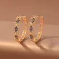 Close-up of gold hoop earrings with blue stones and openwork flower details, displayed as a pair - Deep Blue Flower (E1917) / Gold + Deep Blue