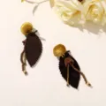 Pair of dark brown leaf earrings with gold ball tops and bead accents on a pale surface - Style 11 (202610)
