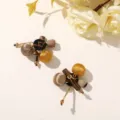 Two fabric-wrapped ornaments with gold and amber beads arranged on a cream surface beside flowers - Style 14 (202610)