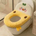Close-up of a plush yellow duck toilet seat cover, embroidered face, green heart and dangling feet - Chicken / Yellow
