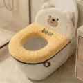 Close-up view of a yellow and cream plush bear-shaped cover fitted over a toilet bowl - Teddy Bear / Yellow