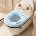 Plush toilet seat cover shown in a bathroom, with a blue ring and cream sheep-shaped backrest - Sheep / Blue