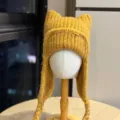 Mustard-yellow rib-knit cat-ear hat with long braided earflap ties, shown on a display form - Adult 54-60 One Size / Yellow