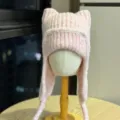 Close-up of a pale pink rib-knit hat with pointed cat ears, long earflaps, and braided ties - Adult 54-60 One Size / Pink