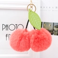 Macro view of plush cherry bag charm with coral faux fur balls and green leaf detail - Orange