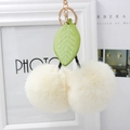 Detail view of plush cherry keychain with soft cream faux fur balls and green leaf charm - Off-white