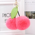 Macro detail of plush cherry keychain with soft pink faux fur balls and green leaves - Watermelon red