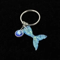 Close-up of gradient resin mermaid tail keychain and fish scale charm on black velvet - Solid Lake Blue