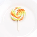 Macro shot of an orange and yellow swirl clay lollipop accessory on a white plate - Orange