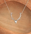 Detailed close-up of a silver reindeer antler pendant on a warm textured wood surface - Silver Necklace