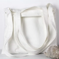 Bolso tote minimalista de lona blanca apoyado en la pared con detalle de caracola - Blanco