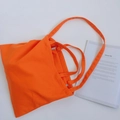 Flat lay of bright orange canvas tote bag next to a magazine on a beige background - Orange