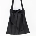 Detalle de bolso tote de lona negra con asas dobles sobre fondo blanco minimalista - Negro