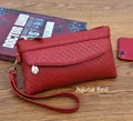 Detail of burgundy woven clutch bag with gold zipper and detachable wrist strap on wood - Wine Red