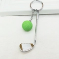 Close-up of a silver golf club and green ball pendant keychain on a white textured surface - Green