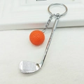 Detail view of silver golf club keychain with orange mini ball on white textured surface - Orange
