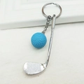 Detail of blue golf ball keychain with silver metal club on white textured fabric - Blue