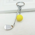 Detail of creative golf club keychain with vibrant yellow ball on textured background - Yellow