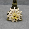 Détail macro d'une broche marguerite en émail avec abeille et finition dorée - Blanc perle