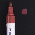Fine fiber tip of terracotta oil-based paint marker showing red-brown ink on black surface - Coffee