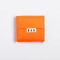 Macro shot of an orange foldable square shopping bag with a white 'BAG' label - Orange