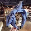 Blue solid fabric wide headband with a large bow detail held in a casual indoor setting - Peacock Blue