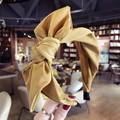 Solid yellow fabric headband with a large bow design shown in a cozy setting - Yellow