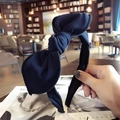 Navy blue fabric headband featuring a large bow knot held in a cozy cafe setting - Navy Blue