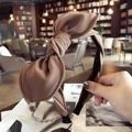 Brown fabric headband with a large bow detail shown in a soft library setting - Coffee