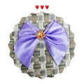 Detail of purple satin bow hair accessory with orange gemstone on a woven mat - Purple