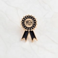 Broche en émail noir et or rose avec texte MEH sur une surface en marbre blanc - Médaille MEH (CC294)