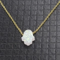 Nahaufnahme der goldenen Hamsa-Hand mit schillerndem weißem Opal auf schwarzem Leder - Weiß