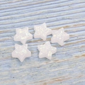 Macro shot of five star-shaped synthetic white opals with iridescent glitters on wood - White