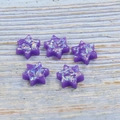 Cinque ciondoli a stella in opale sintetico viola su uno sfondo con venature di legno chiaro - Viola