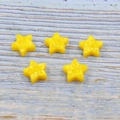 Close-up of five yellow resin star-shaped beads with 1.5mm holes on a wood surface - Yellow