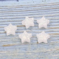 Detail of five white synthetic opal star beads with colorful luster on wood surface - White