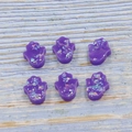 Makro-Detail von sechs lila Hamsa-Hand-Opalperlen mit schillernden Flocken auf Holzoberfläche - Lila
