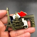 Detailed close-up of a bronze Paris souvenir fridge magnet held by hand for scale - France Panorama 2