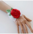 Detail of red satin rose wrist corsage with lace, white pearls, and green leaves - Red