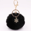 Macro detail of black faux fur pompom and golden snowflake alloy charm on keychain - Black