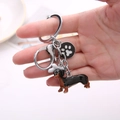 Creative metal keychain featuring dachshund, bone and footprint charms held in hand - Dachshund