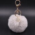 Detailed view of grey plush pompom keychain with golden snowflake charm and lobster clasp - Grey/White
