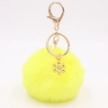 Macro detail of plush yellow pom-pom keychain with golden alloy snowflake charm - Yellow