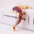 Golden dolphin keychain with purple and white rhinestones on a decorative book background - Purple